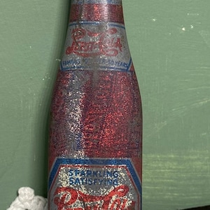 May include: Vintage Pepsi-Cola bottle with a red and blue color scheme. The bottle has the Pepsi-Cola logo and text that reads "Famous for over 50 years". The bottle is an advertising novelty.