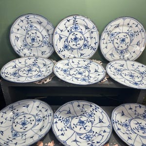 May include: A collection of white porcelain plates with a blue floral design. The plates vary in size and are arranged on a dark surface. The blue pattern includes flowers and intricate details, creating a classic aesthetic.