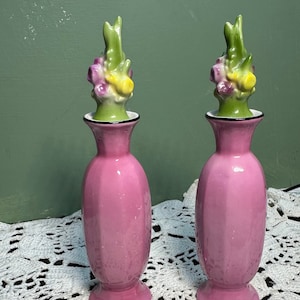 May include: Two pink ceramic vases with floral tops. The tops are green with yellow and purple flowers. The vases have a textured surface.