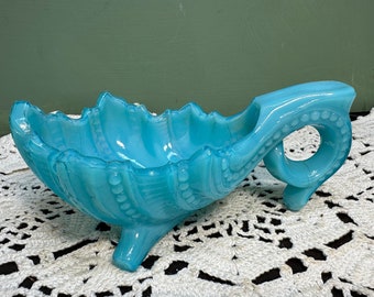 May include: A turquoise blue glass dish with a scalloped edge and a handle shaped like a curled tail. The dish has a three-legged base and is decorated with raised beads.