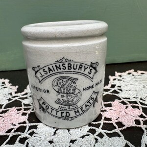 May include: White ceramic jar with black lettering that reads "J. Sainsbury's Superior Home Made Potted Meats". The jar has a textured surface and a black and white logo with a stylized "S" in the center.