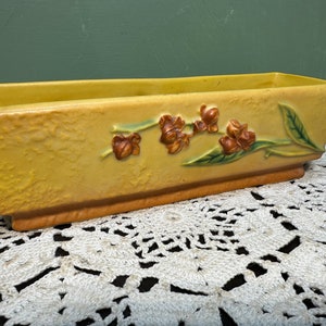 May include: A yellow planter with a brown floral design. The planter has a textured surface and a rectangular shape.