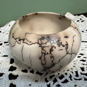 May include: A small, white ceramic bowl with a black crackle glaze design. The bowl is round and has a slightly flared rim.