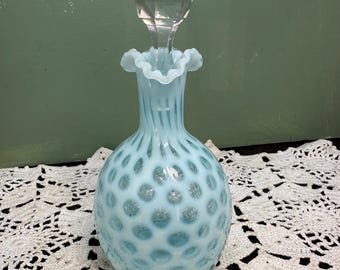 May include: A light blue glass bottle with a textured, bubble-like surface. The bottle has a clear glass stopper with a faceted design.