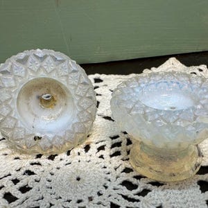 May include: Two white opalescent glass candle holders with a diamond pattern. The candle holders have a small base and a wide, shallow bowl.
