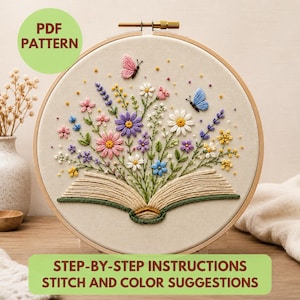 以下が含まれることがあります： 刺繍枠には、開いた本から色とりどりの野花と2匹の蝶が飛び出している刺繍デザインが施された布パネルが入っています。PDF PATTERNおよびSTEP-BY-STEP INSTRUCTIONS STITCH AND COLOR SUGGESTIONSというテキストが表示されています。