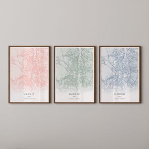 May include: Three framed city map prints of Madrid, Spain, in shades of pink, green, and blue. Each print features a detailed street map design with the city name and coordinates at the bottom. The frames are a dark brown color.