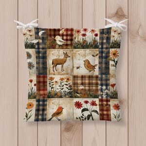 May include: A square seat cushion featuring a patchwork design of plaid patterns and nature-themed illustrations including a deer, various birds, and colorful flowers. The cushion has white fabric ties at the top corners for securing it to a chair.