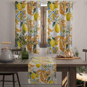 Puede incluir: Cortinas blancas, un camino de mesa y un mantel con un diseño de limón y flores. El diseño presenta limones amarillos, flores blancas y volutas doradas sobre un fondo blanco. Las cortinas cuelgan frente a una ventana.