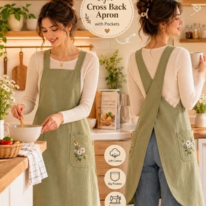 May include: A sage green cross-back apron featuring embroidered daisy floral patterns on the front pockets. The apron has wide shoulder straps that cross in the back and a square neckline. Text on the image reads Stylish Cross Back Apron with Pockets.