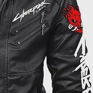 Może przedstawiać: Czarna kurtka ze sztucznej sk&oacute;ry z wieloma kieszeniami zapinanymi na zamek i białym napisem "Cyberpunk 2077". Posiada czerwoną naszywkę z demonem na rękawie i biały tekst wzdłuż ramienia. Kurtka ma klasyczny styl motocyklowy.