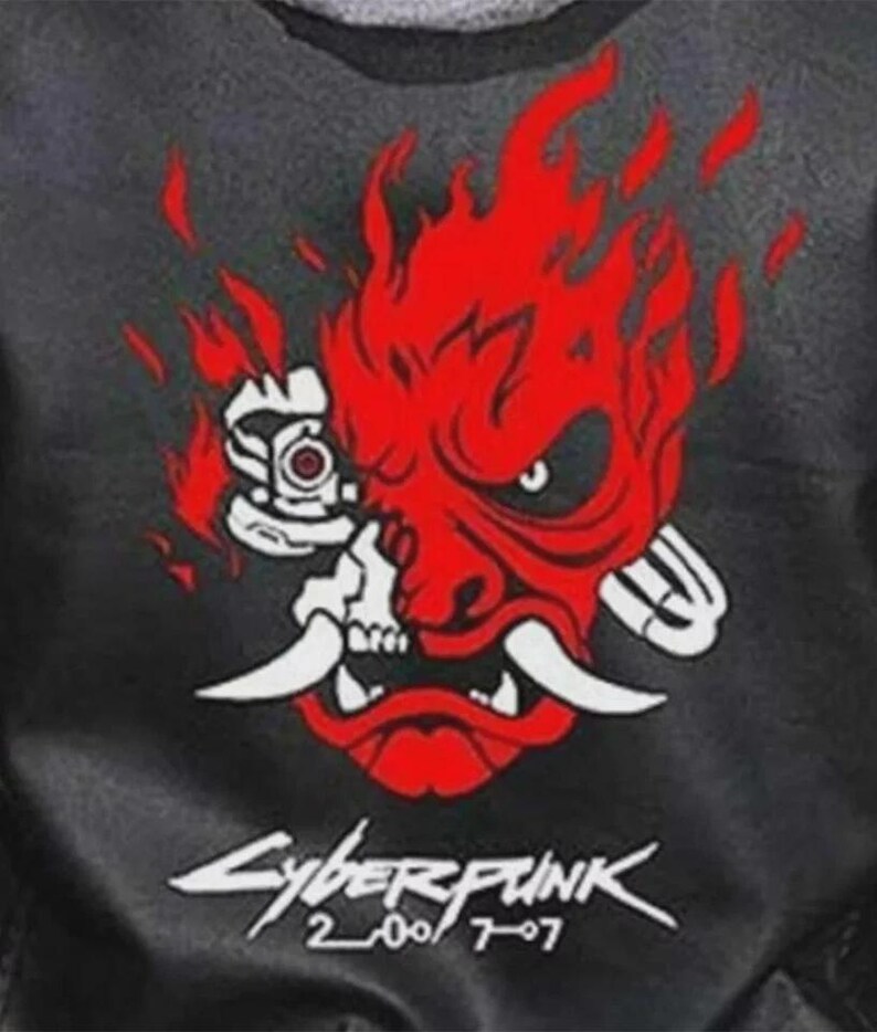 Może przedstawiać: Czarna kurtka z czerwono-białą grafiką stylizowanej twarzy demona z płomieniami. Tekst "Cyberpunk 2077" jest wydrukowany poniżej na biało, z numerami "2007" i "707".