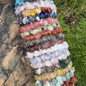 Può includere: Una collezione di braccialetti con schegge di pietre preziose in vari colori, tra cui turchese, trasparente, giallo, rosso, blu, rosa e verde. I braccialetti sono impilati, mostrando la varietà di pietre.