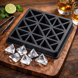 Puede incluir: Una cubitera de silicona negra con un diseño triangular geométrico, que produce cubitos de hielo en forma de pirámide. La cubitera está sobre una tabla de cortar de madera, con varios cubitos de hielo piramidales.