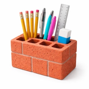 Può includere: Un organizer da scrivania a forma di mattone, in materiale rosso-arancio, contenente matite gialle, penne, un righello e una gomma blu e bianca. L'organizer ha diverse aperture quadrate.