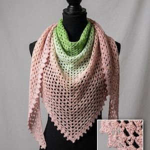 May include: A handmade crochet shawl in a triangular shape, displayed on a black mannequin. The shawl features a gradient of colors, starting with green at the neck, transitioning to white, then peach, and finally pink. The edges have a scalloped design.