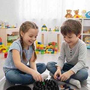 Peut inclure: Deux enfants jouent à un jeu de chevilles noir avec des chevilles colorées. Le jeu est sur une surface grise. Les enfants portent des jeans bleus et sourient. Des jouets et une table en bois sont à l'arrière-plan.