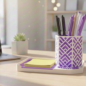 Peut inclure: Un organiseur de bureau blanc et violet avec des stylos, des crayons et des post-it. L'organisateur présente un motif géométrique et une base rectangulaire. Un ordinateur portable et une petite plante sont également sur le bureau.