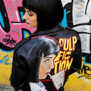 May include: Black leather jacket with a hand-painted design of a woman smoking, and the words "PULP FICTION" in yellow and red. The jacket has a classic biker style with a collar and shoulder epaulettes. The background is a colourful graffiti wall.