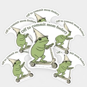 May include: A collection of stickers featuring a green frog riding a scooter and wearing a pointed hat. The text "Off to commit mom foolery" is printed around the frog. The stickers have a white border.