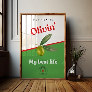 May include: A framed poster with a green and white background, featuring the text "Muy Picante" and "Olivin'" in red. An olive branch with a single olive is in the center. The phrase "My best life" is below the olive branch.