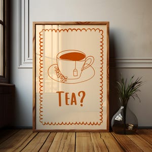 Op de afbeelding: Een ingelijste print met een minimalistische illustratie van een theekopje met een theezakje, op een schotel met bloemmotieven. De tekst "TEA?" staat eronder. Het kunstwerk is in oranje- en crèmetinten.