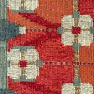 May include: A woven textile featuring a geometric pattern of white, four-petaled floral shapes with red centres and blue-grey accents. The background consists of alternating blocks of vibrant orange and deep red, with a blue-grey vertical border.