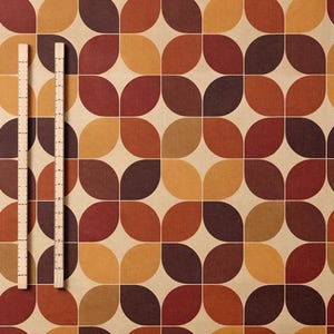 May include: A patterned fabric featuring a repeating design of rounded shapes in shades of brown, orange, and tan. Two wooden rulers are placed vertically on the left side of the fabric. The design evokes a retro or mid-century modern aesthetic. The rulers provide scale.