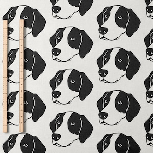 Può includere: Tessuto bianco con un motivo ripetuto di facce di cani in bianco e nero. I cani hanno orecchie e segni sul viso neri. Due righelli di legno sono posizionati verticalmente sul lato sinistro del tessuto.