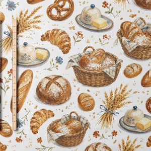 May include: A fabric pattern featuring illustrations of bread loaves, croissants, pretzels, butter dishes, and wheat stalks. A wooden ruler is visible on the left side, showing a length of 12 inches for the scale of the printed pattern.