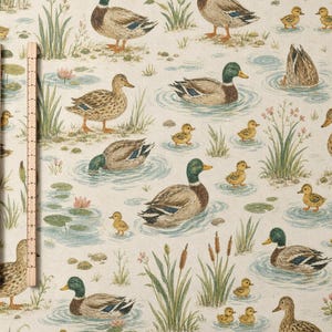 May include: A light beige fabric featuring a repeating pattern of mallard ducks and ducklings swimming in blue water among green reeds and pink water lilies. A wooden ruler is placed vertically on the left side to show scale in centimetres.