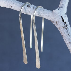 May include: A pair of silver dangle earrings with a hammered finish. The earrings are hanging from a branch.