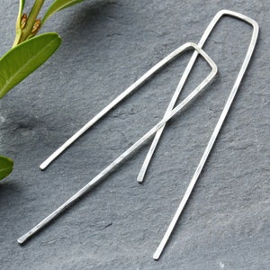 May include: A pair of long, silver earrings with a rectangular shape. The earrings are made of hammered metal and have a simple, modern design.
