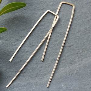 Peut inclure: Une paire de longues boucles d'oreilles fines de couleur or avec une forme rectangulaire. Les boucles d'oreilles sont en métal et ont un design simple et minimaliste.