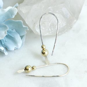 May include: A pair of silver hoop earrings with gold beads. The earrings are simple and elegant, and would make a great gift for any occasion.