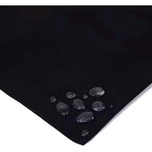 Puede incluir: Primer plano de una tela negra texturizada con gotas de agua en la superficie. La tela parece ser resistente al agua, con las gotas perladas en el material. La imagen destaca la textura de la tela y su capacidad para repeler el agua.