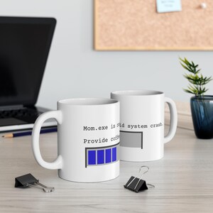 May include: Two white ceramic coffee mugs with black text. One mug reads "Mom.exe is mid system crash. Provide coffee" with a blue loading bar. The other mug reads "system crash" with a gray loading bar.