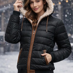 May include: Black puffer jacket with a faux fur-lined hood and brown trim. The jacket features a zip-up front, pockets, and a ribbed knit cuff. The model is wearing blue jeans. The jacket is designed for cold weather.