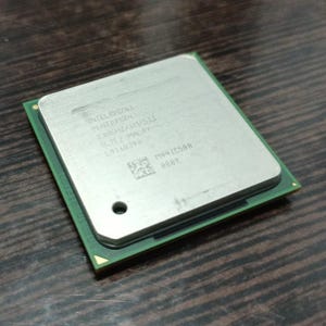 Peut inclure: Un processeur d'ordinateur argenté et vert, probablement un CPU Intel, avec du texte et un petit trou. Le processeur est posé sur une surface en bois sombre. Le dessus du processeur est argenté avec du texte imprimé.