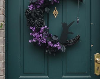 Gotische krans in de vorm van een halve maan met zwarte rozen en paarse bloemen, heksenachtige voordeurdecoratie, donkere Halloween-decoratie voor de entree.