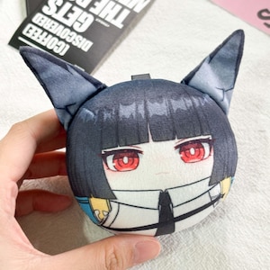 May include: A round plush toy featuring a character with short black hair, pointed cat-like ears, and bright red eyes. The character wears a white collared shirt with a black tie and blue accents. The plush has a soft, smooth texture.