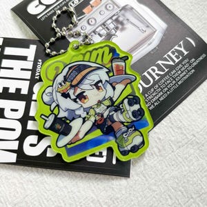 May include: A lime green acrylic keychain featuring a cartoon character with white hair, wearing a cap and roller skates, holding a tray with a drink. The character has a yellow and black design on the cap. A silver metal ball chain is attached.