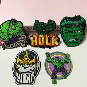 Puede incluir: Parches bordados con varios diseños de Hulk y Thanos. Los parches de Hulk muestran al personaje en diferentes poses y expresiones, con colores verdes y morados vibrantes. El parche de Thanos presenta un diseño detallado con detalles amarillos y negros.