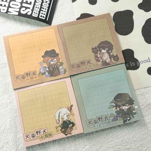 May include: Four square sticky note pads featuring anime-style character illustrations. Each pad has a grid pattern, a unique pastel background color, and Japanese text. The characters are depicted in various outfits, including hats and traditional garments.