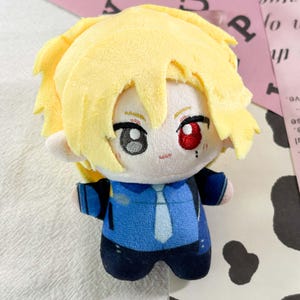 May include: A plush doll featuring bright yellow hair, a pale complexion, and heterochromia with one grey eye and one red eye. The doll wears a blue collared shirt with a white tie and dark blue trousers, crafted from soft fabric with embroidered details.