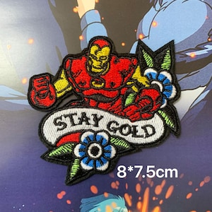 Könnte beinhalten: Gestickter Aufnäher mit Iron Man in Rot und Gelb, mit dem Schriftzug "STAY GOLD" auf einem Banner. Der Aufnäher enthält blaue und rote Blumenmotive und misst 8 x 7,5 cm.