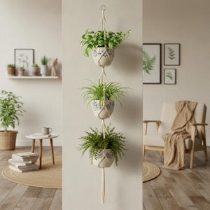 May include: A three-tiered hanging planter with three ceramic pots filled with greenery. The pots are cream-colored with blue floral designs and are suspended by off-white macrame cords. The background includes a neutral-toned wall and decor.