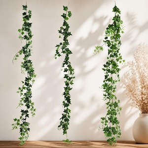 May include: Three hanging artificial ivy garlands featuring realistic green leaves with light-colored veins. Each vine displays a cascading structure with multiple stems and pointed foliage, creating a dense, trailing appearance for decorative display.