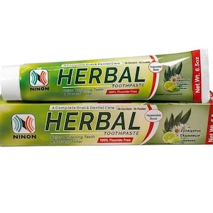 May include: Herbal Toothpaste tube, with a green and white design. The packaging includes the brand name NINON and highlights features like whitening and tartar prevention. The box also features eucalyptus, chamomile, and limonene. Net weight is 184 grams.