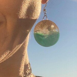 Puede incluir: Una taza de cerámica blanca con asa negra y el texto "But First, Coffee" en negrita negra. La taza se encuentra sobre un fondo borroso, sugiriendo un ambiente acogedor.